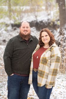Man and woman stand with arms around each other as snow falls.