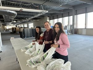 Three women pack plastic bags with items.