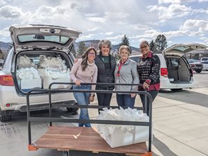 Four women stand with a cart in front of an SUV packed with bags.