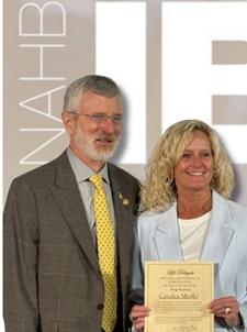 Man and woman stand side-by-side while woman holds award certificate.