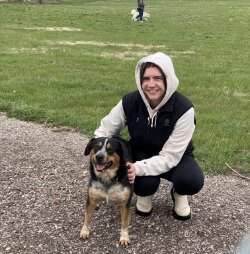 Woman squats by black, white, and brown medium-sized dog.
