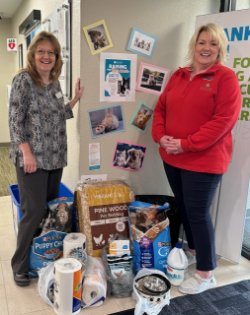 Two women stand and smile by a pile of pet supply donations.